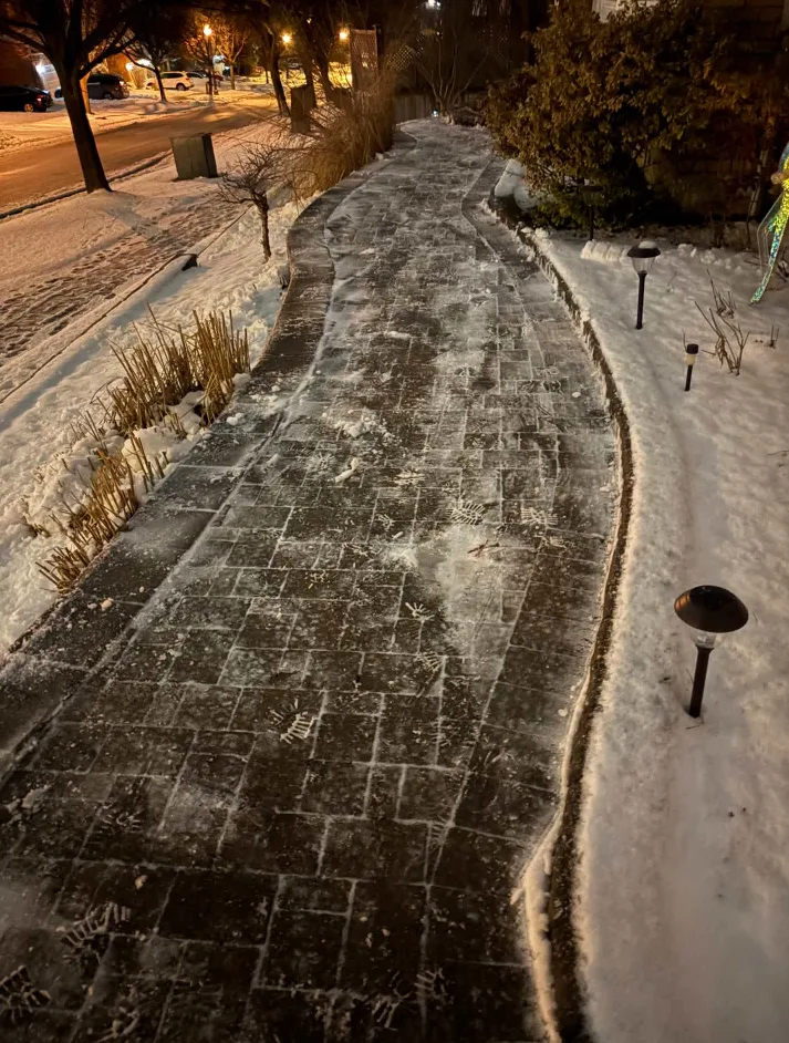 Curved paver walkway cleared of snow beside a residential street at night in Durham Region, Ontario