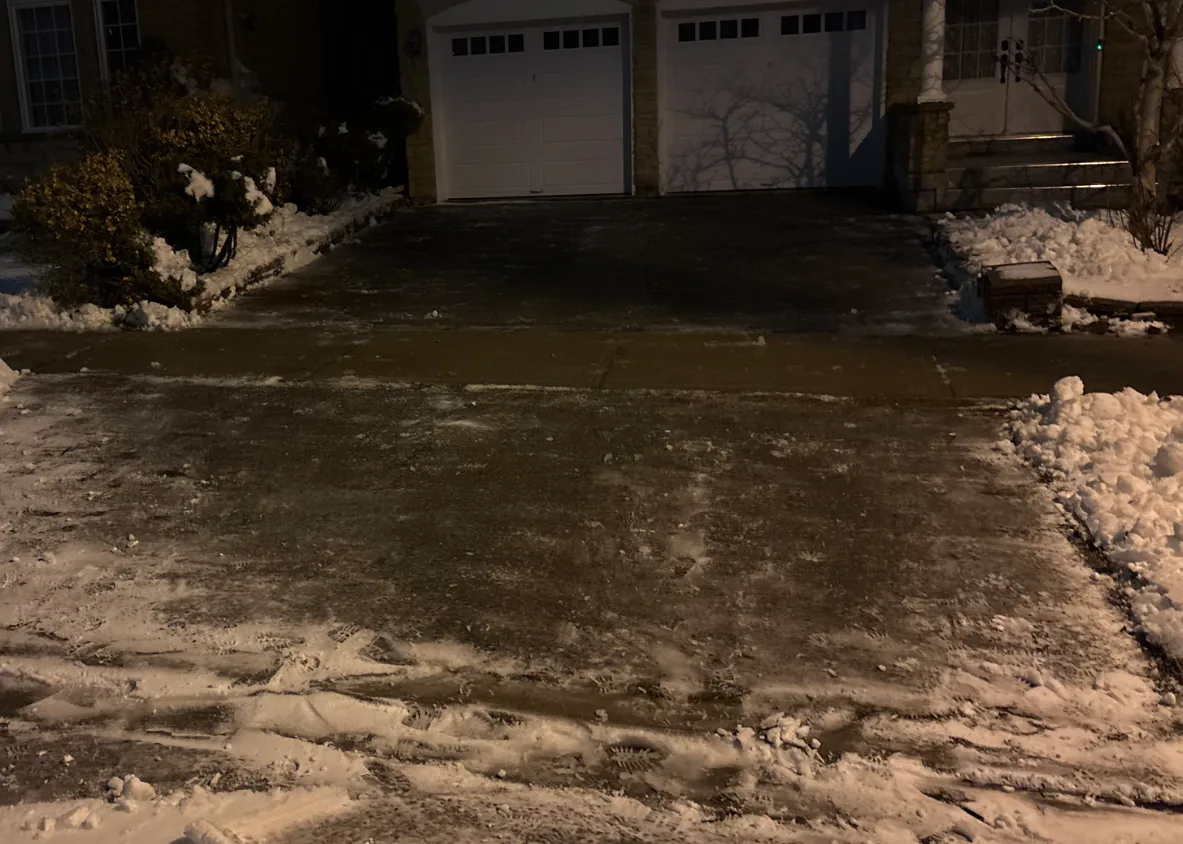 Driveway cleared of snow leading to a double garage beside front steps in Toronto, Ontario
