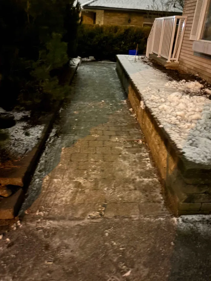 Narrow side walkway cleared of snow beside a brick home and raised garden bed in Durham Region, Ontario